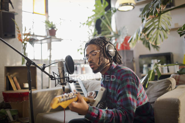 Jovem músico masculino gravando música, tocando guitarra no microfone no apartamento — Fotografia de Stock