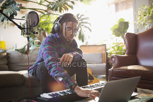 Молодой музыкант записывает музыку, используя ноутбук и клавишное фортепиано — стоковое фото