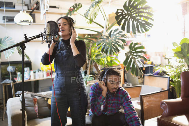 Young man and woman recording music in apartment, singing into microphone — Stock Photo