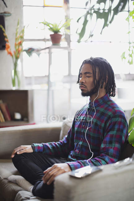 Serene young man meditating with headphones in armchair — Stock Photo