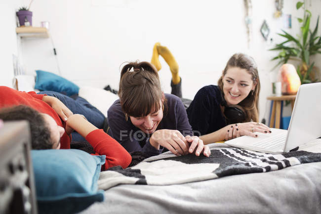 Ridere giovani donne amiche con computer portatile sul letto — Foto stock