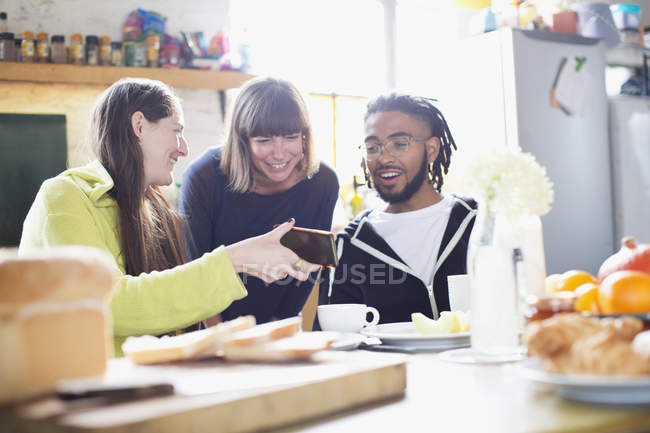 Young roommate friends using smart phone at breakfast table in apartment — Stock Photo