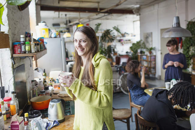 Усміхнена молода жінка п'є каву з сусідами в квартирі кухні — стокове фото