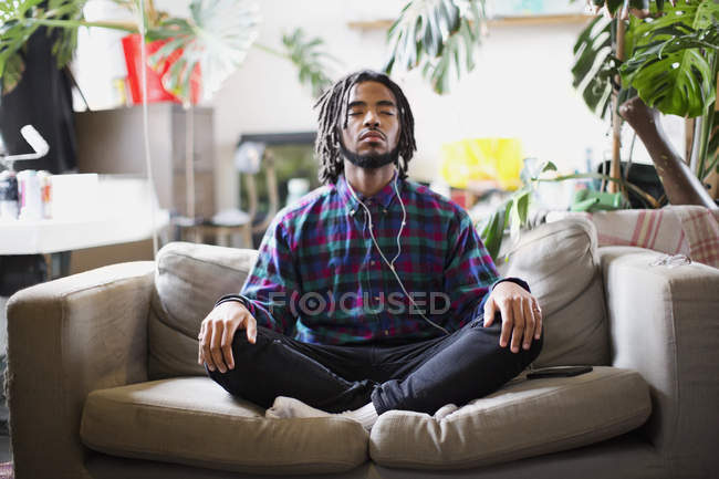 Serene young man meditating with headphones on apartment sofa — Stock Photo