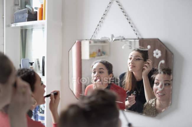 Young women friends getting ready, applying makeup in bathroom mirror — Stock Photo