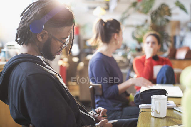 Young man with headphones studying at kitchen table — Stock Photo