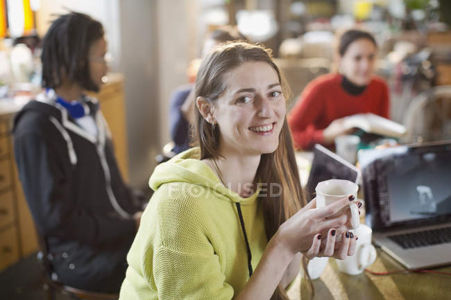 Портрет уверенной молодой женщины, пьющей кофе за кухонным столом с соседями — стоковое фото