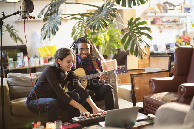 Giovani uomini e donne che registrano musica, suonano chitarra e pianoforte a tastiera in appartamento — Foto stock