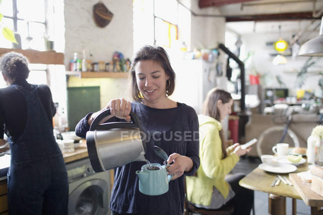 Junge Frau gießt heißes Wasser in Teekanne in Wohnküche — Stockfoto