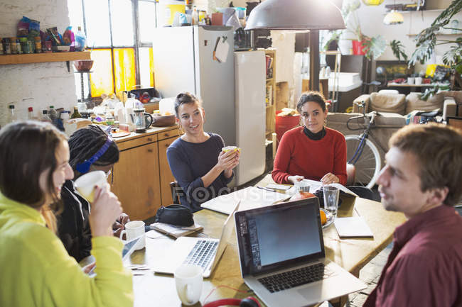 Молодые друзья студента колледжа учатся за кухонным столом в квартире — стоковое фото