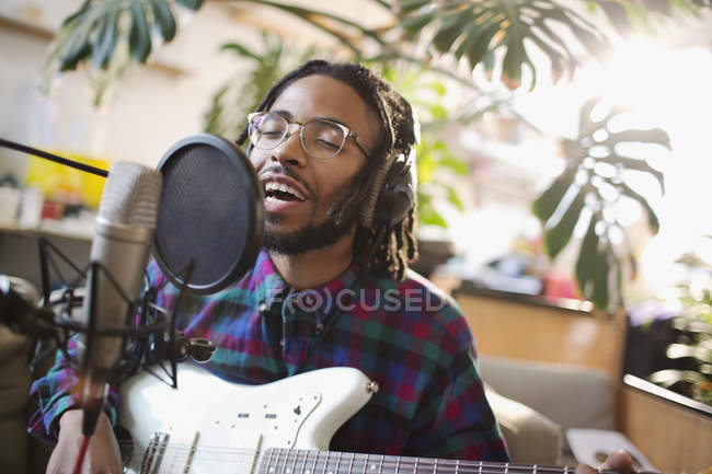 Молодой человек записывает музыку, играет на гитаре и поет в микрофон — стоковое фото