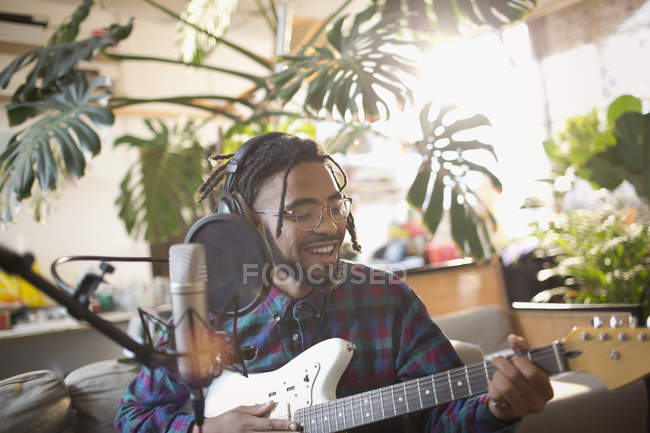 Young man recording music, playing guitar and singing into microphone — Stock Photo