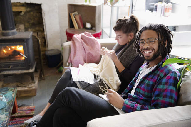 Portrait smiling young man writing in notebook on sofa next to girlfriend knitting — Stock Photo