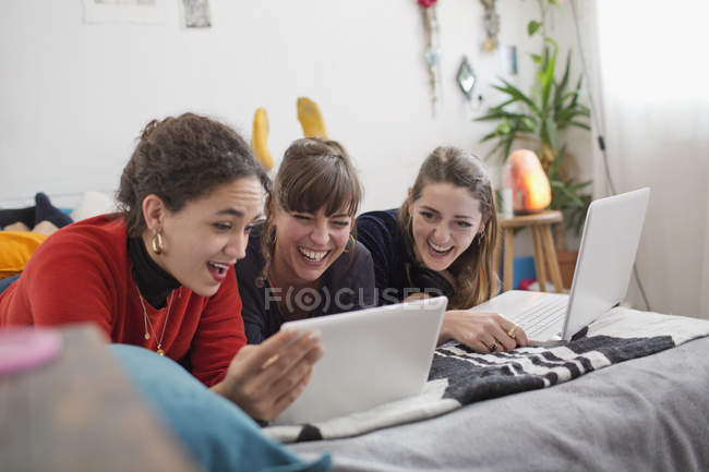 Jovens amigas saindo, usando tablet digital e laptop na cama — Fotografia de Stock