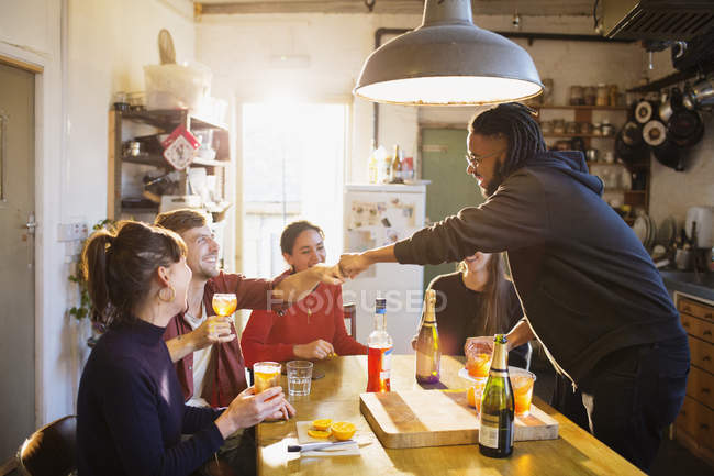 Young adult friends enjoying cocktails, fist bumping at apartment kitchen table — Stock Photo