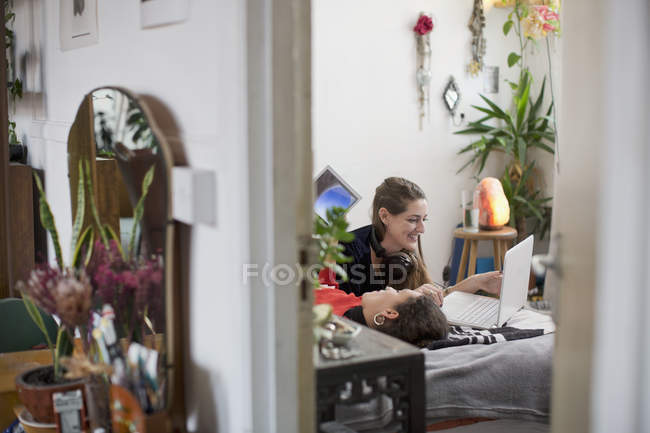 Young women friends relaxing, using laptop and digital tablet on bed — Stock Photo