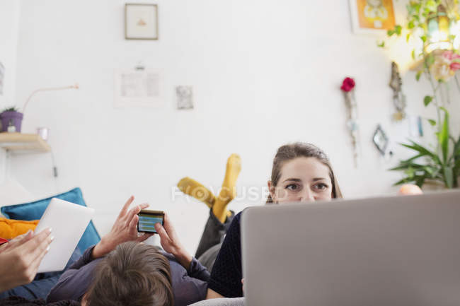 Las mujeres jóvenes que relajan, usando el ordenador portátil, teléfono inteligente y tableta digital en la cama - foto de stock