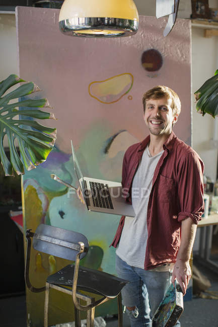 Retrato artista masculino com laptop em grande pintura — Fotografia de Stock