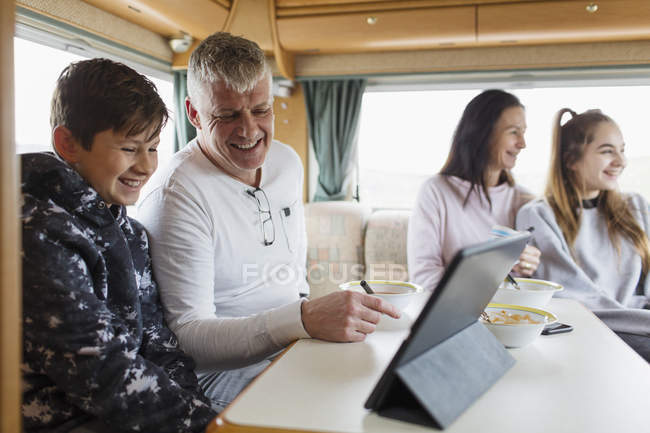 Family relaxing, eating breakfast and using digital tablet in motor home — Stock Photo