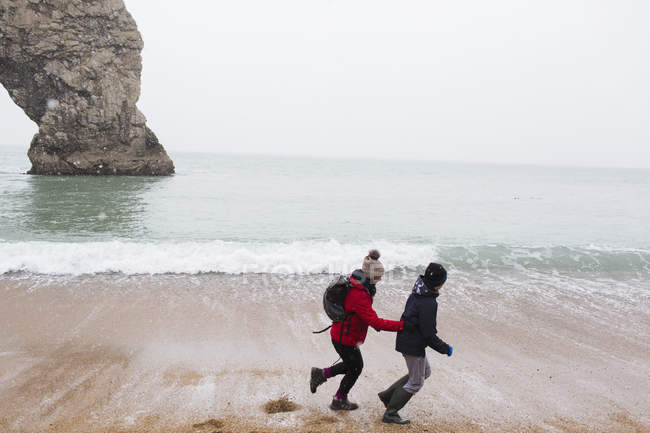 Madre e figlio che corrono sulla spiaggia invernale innevata — Foto stock