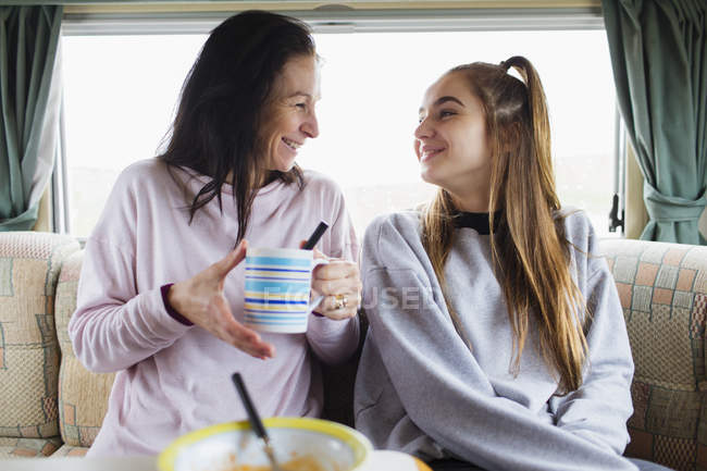 Feliz madre e hija disfrutando de chocolate caliente en autocaravana - foto de stock
