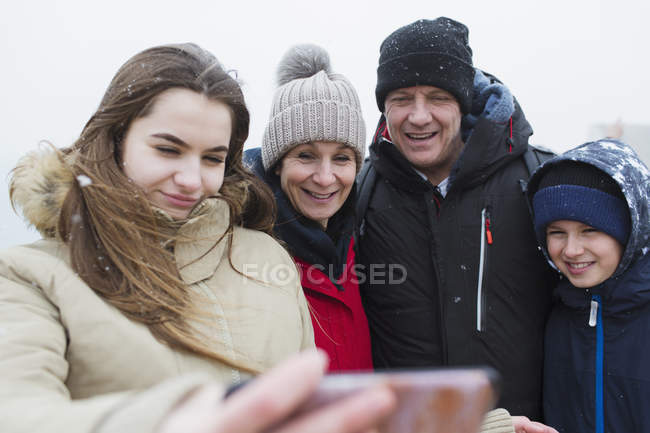 Снег падает на улыбающуюся семью, делая селфи — стоковое фото
