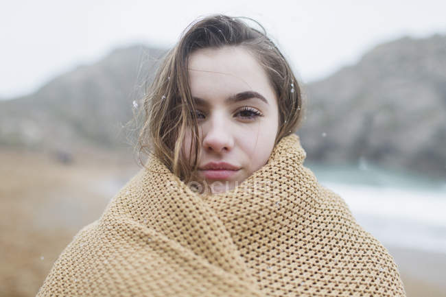 Retrato confiante, menina séria com neve no cabelo envolto em cobertor na praia de inverno — Fotografia de Stock