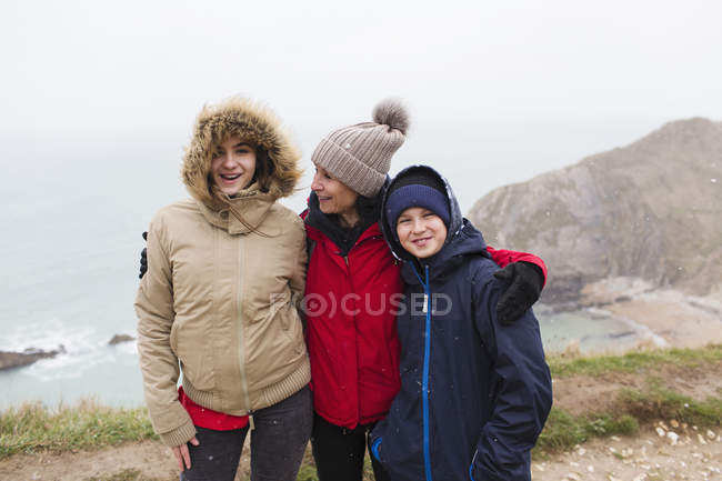 Portrait happy family in warm clothing standing on cliff overlooking ocean — Stock Photo