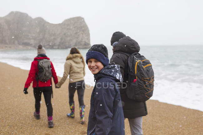 Portrait garçon heureux marchant sur la plage enneigée de l'océan d'hiver en famille — Photo de stock