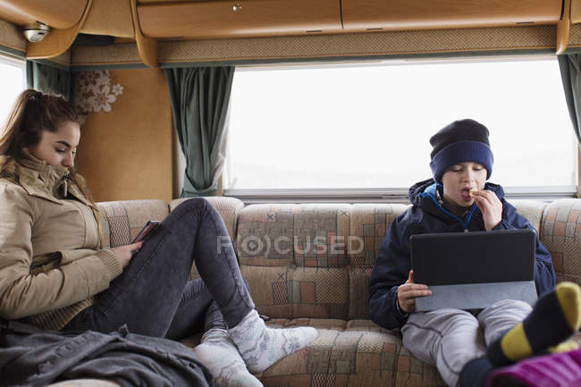 Irmão adolescente e irmã usando tablet digital e telefone inteligente em casa de motor — Fotografia de Stock