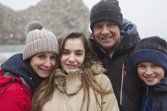 Снег падает на улыбающуюся семью, позируя в теплой одежде — стоковое фото