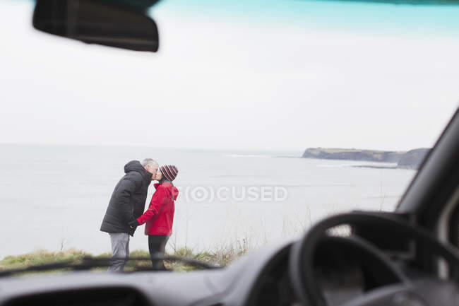 Ласковая пара целуется у дома на колесах на скале с видом на океан — стоковое фото