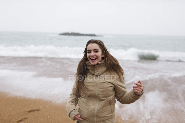 Portrait happy, carefree teenage girl on snowy winter beach — Stock Photo