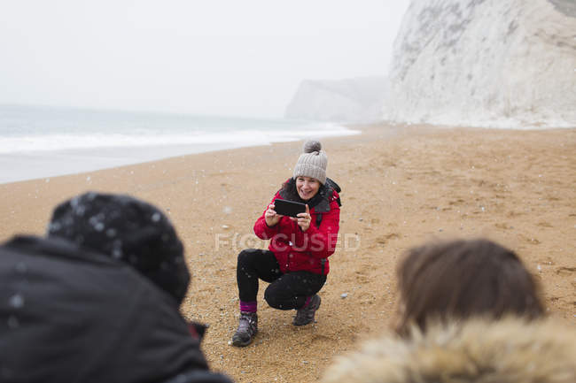 Madre con fotocamera telefono fotografare i bambini sulla spiaggia invernale innevata — Foto stock