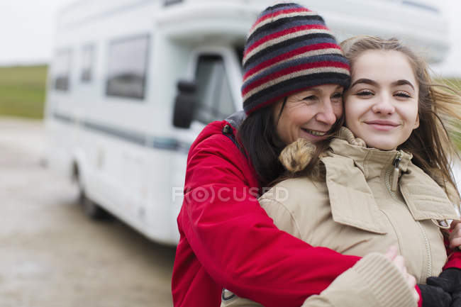 Прихильна мати і дочка в теплому одязі обіймаються поза мотором будинку — стокове фото