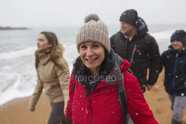 Портрет усміхненої жінки в теплому одязі з сім'єю на засніженому пляжі зимового океану — стокове фото