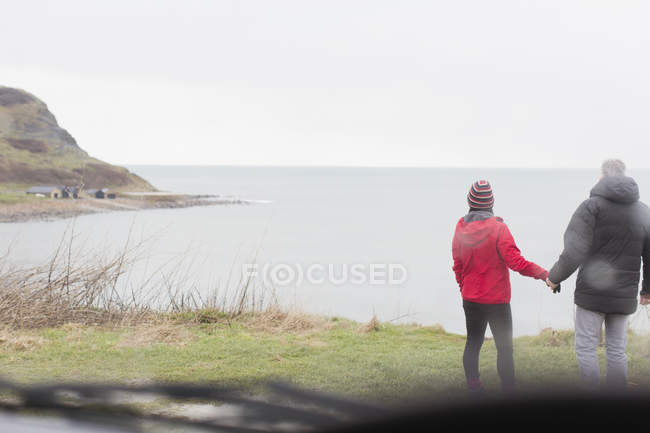 Пара тримає руки на скелі з видом на океан — стокове фото