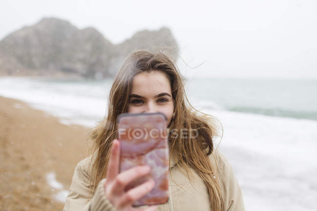 Дівчина-підліток з телефоном знімає селфі на пляжі зимового океану — стокове фото