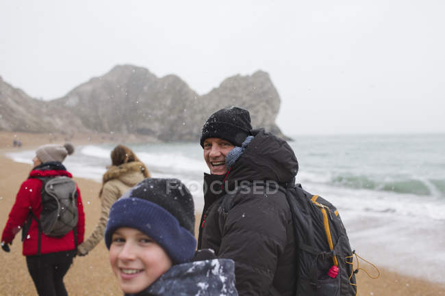 Porträt Vater und Sohn in warmer Kleidung beim Spazierengehen am schneebedeckten winterlichen Meeresstrand — Stockfoto