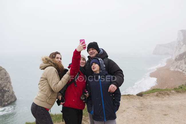 Familia con teléfono de cámara tomando selfie en el acantilado con vistas al océano - foto de stock