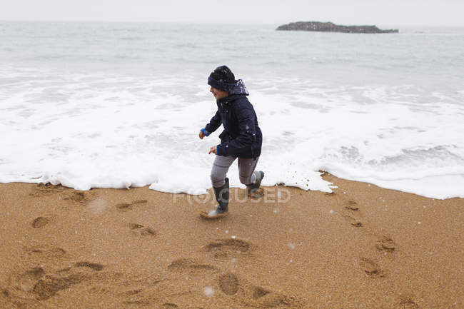 Играющий мальчик играет в зимний океанский серф — стоковое фото