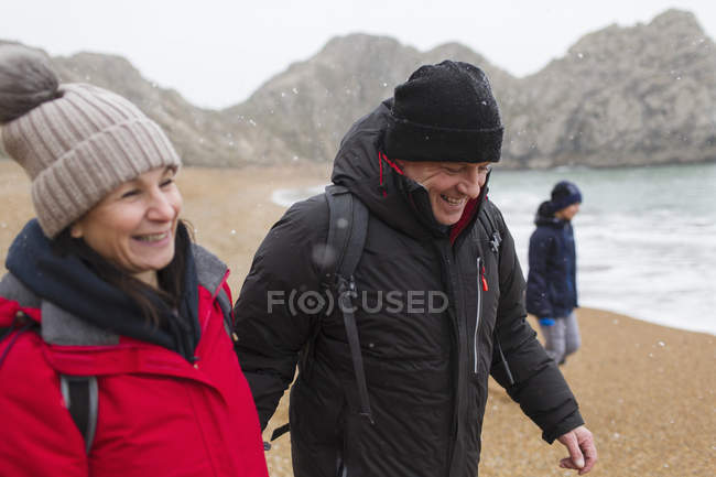 Smiling couple in warm clothing on snowy winter beach — Stock Photo