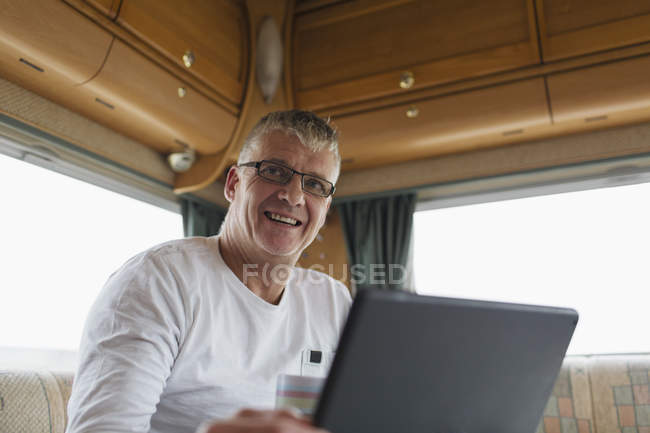 Un homme souriant et confiant qui boit du café et utilise une tablette numérique dans un camping-car — Photo de stock