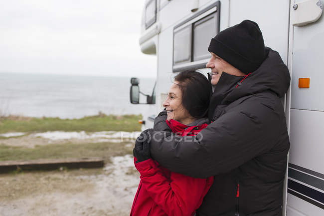 Liebevolles Paar in warmer Kleidung umarmt sich vor Wohnmobil — Stockfoto