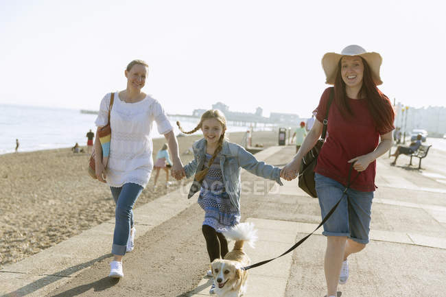 Lesbian couple walking with daughter and dog on sunny beach boardwalk — Stock Photo