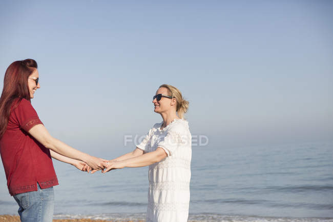 Cariñosa pareja lesbiana cogida de la mano en la soleada playa del océano - foto de stock