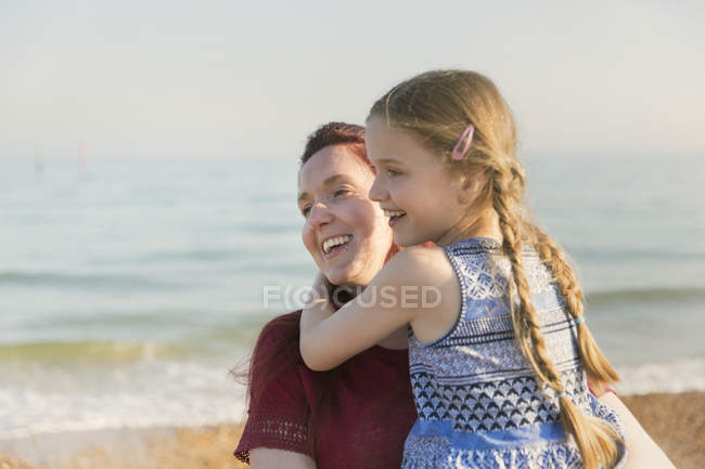 Mãe afetuosa segurando filha na praia ensolarada — Fotografia de Stock