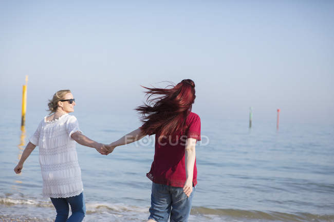 Affectionate lesbian couple holding hands on sunny ocean beach — Stock Photo