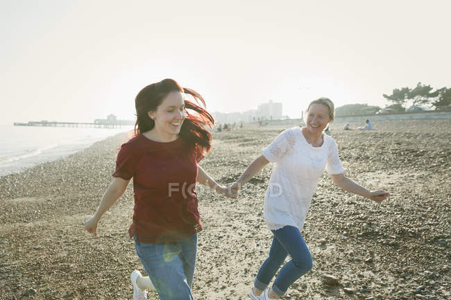 Грайлива, ласкава лесбійська пара тримає руки і бігає на сонячному пляжі — стокове фото