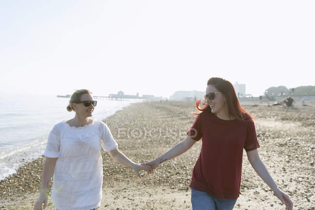 Cariñosa pareja lesbiana cogida de la mano en la soleada playa - foto de stock